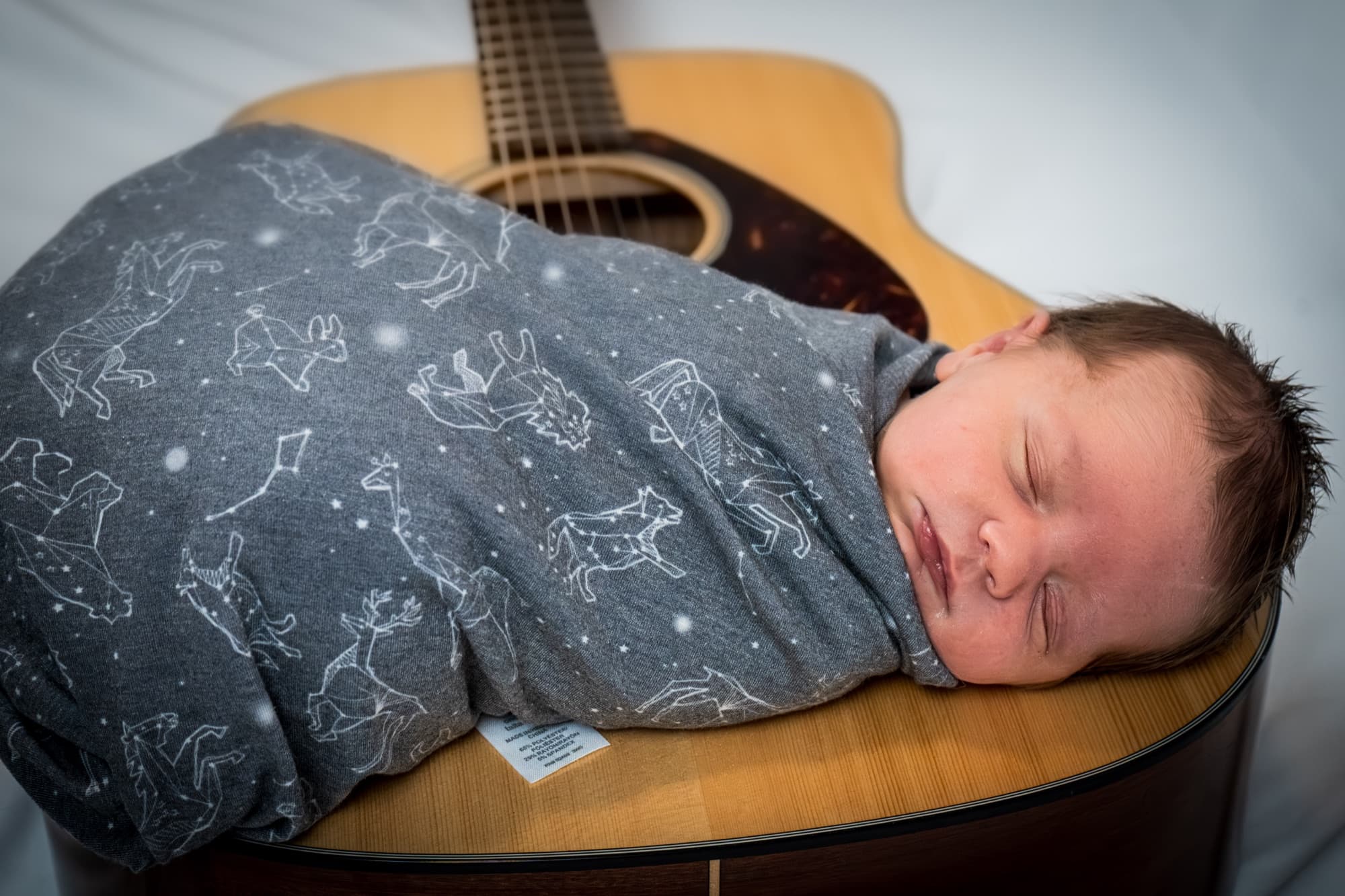 Newborn in a constellation swaddle asleep on an acoustic guitar