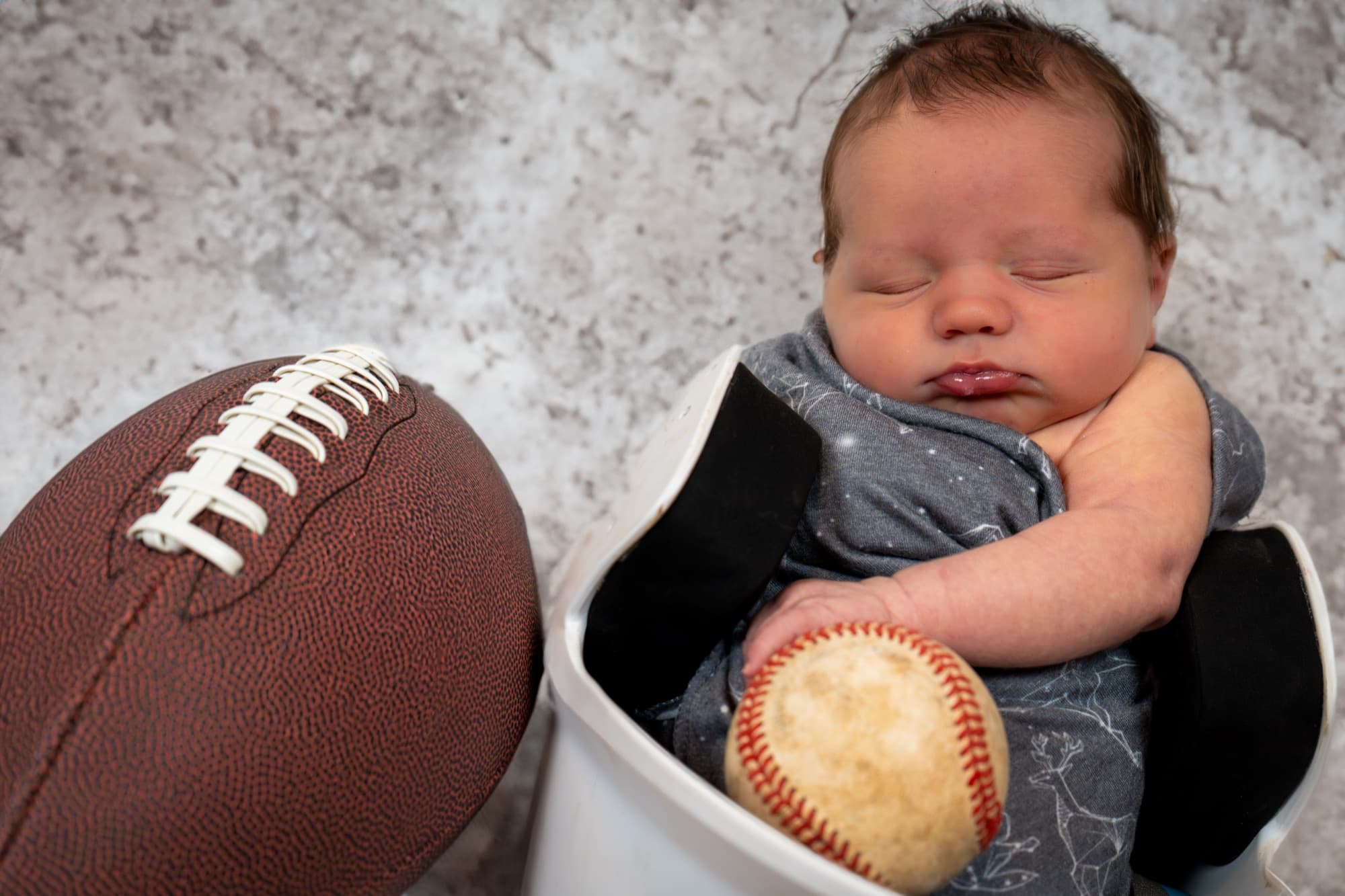 Newborn asleep beside a football and a baseball