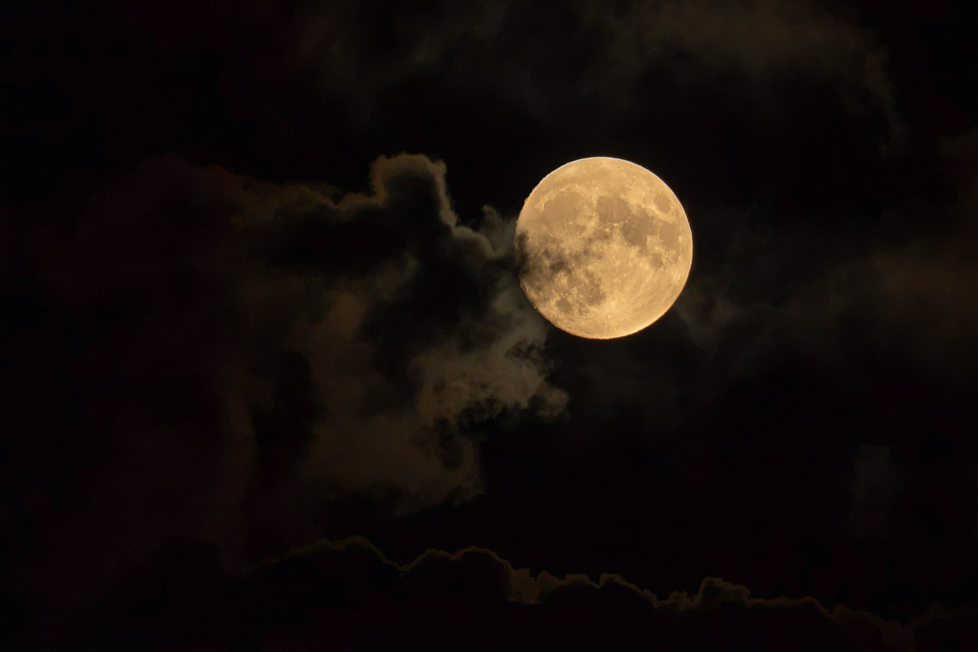 Full moon glowing through a break in dark clouds